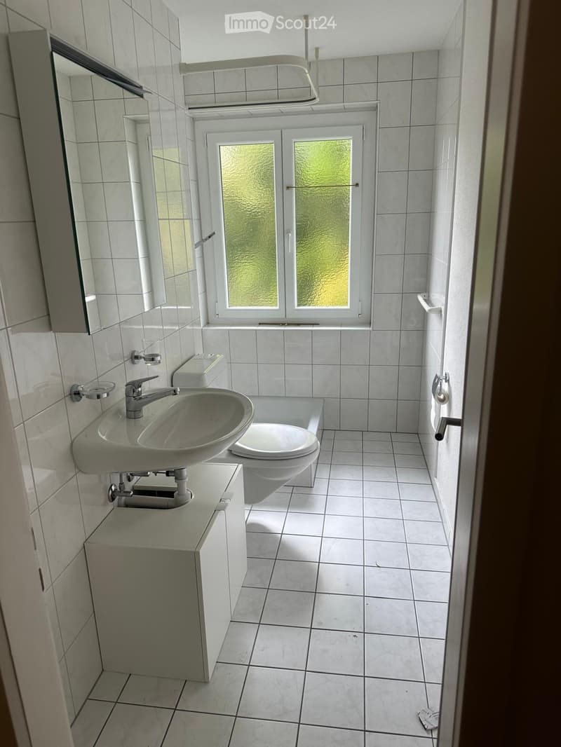 Clean, modern bathroom with white tiles, a sink with a modern faucet, a toilet, a mirror, and a small cabinet.