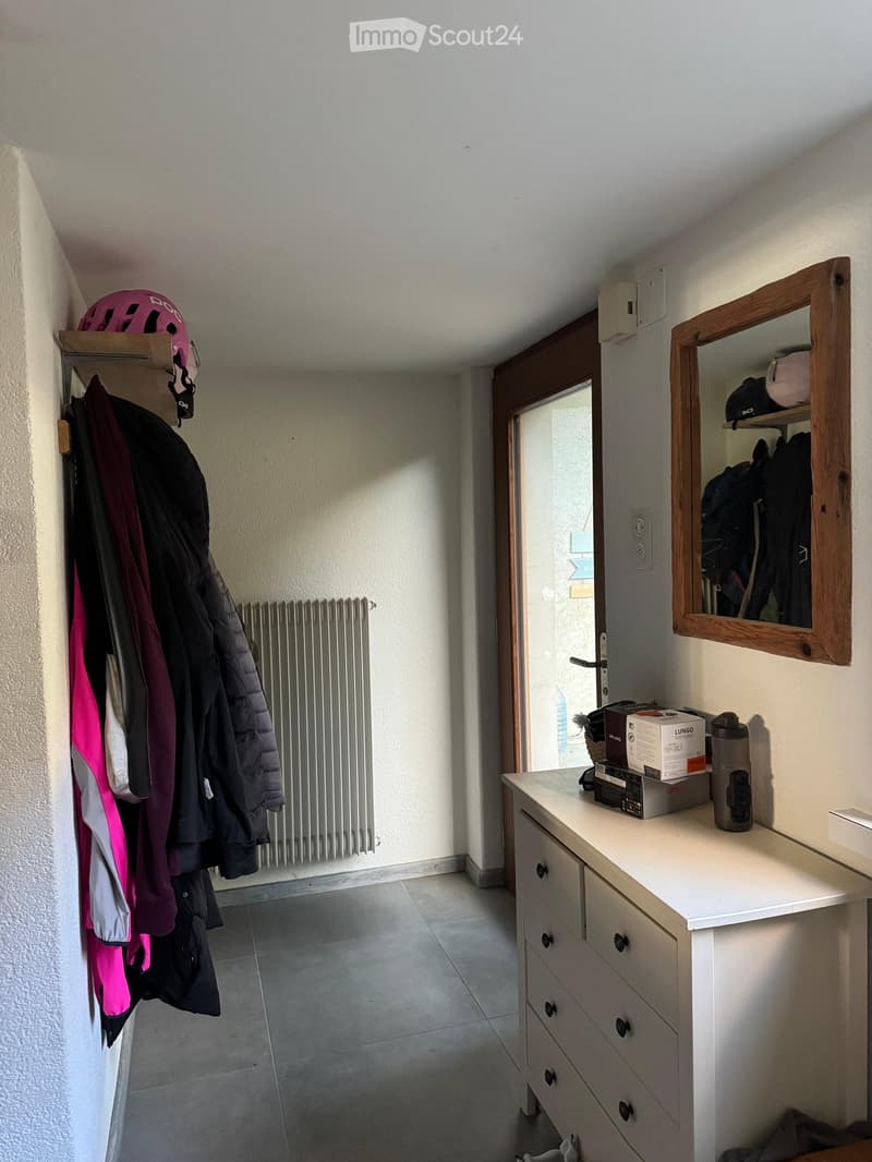 A small hallway with a coat rack, a mirror, a drawer unit, and a radiator. A helmet is placed on top of the coat rack.