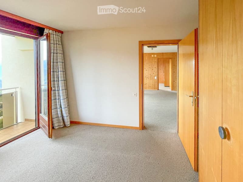Empty hallway with carpeted floor, wooden doors, and a window with striped curtains leading to a balcony area.