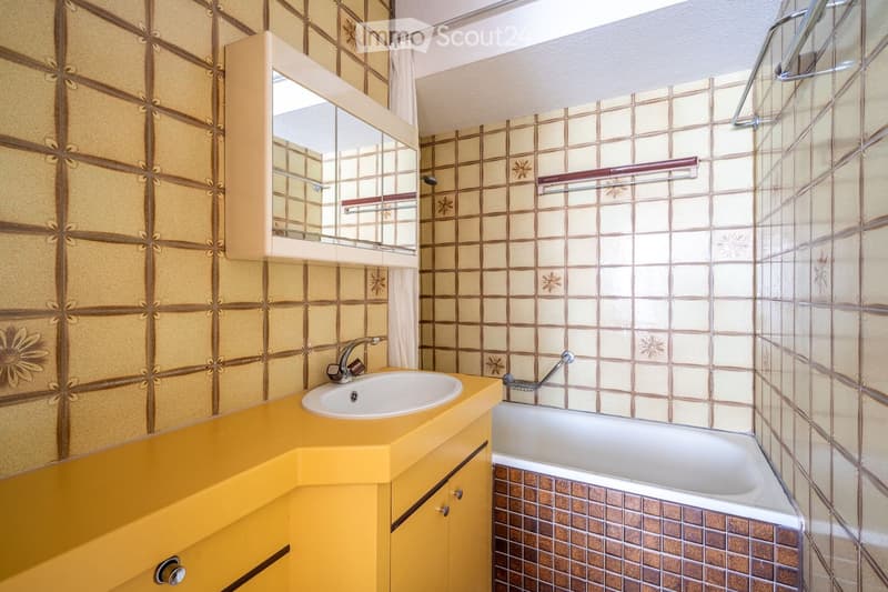 Bathroom with yellow cabinetry, white sink, bathtub, and floral-patterned tiles.