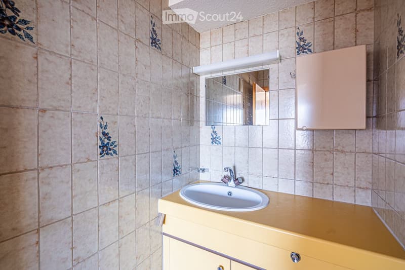 Bathroom with beige tiled walls, a yellow countertop, a white sink, a mirror above the sink, and a light fixture above the mirror.