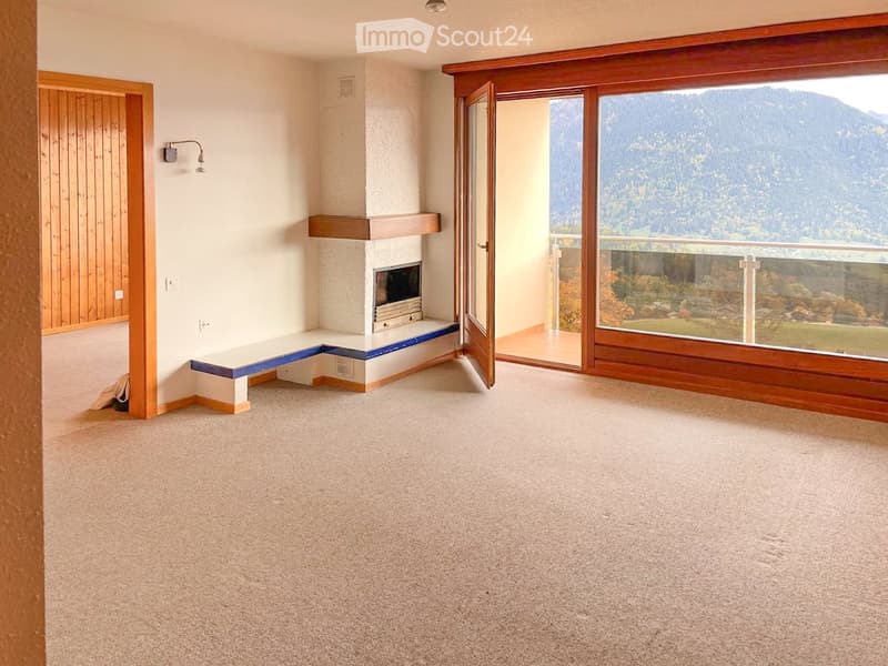 Empty room with carpeted floor, fireplace with built-in seating, large window with scenic mountain view, and open sliding glass door leading to a balcony.