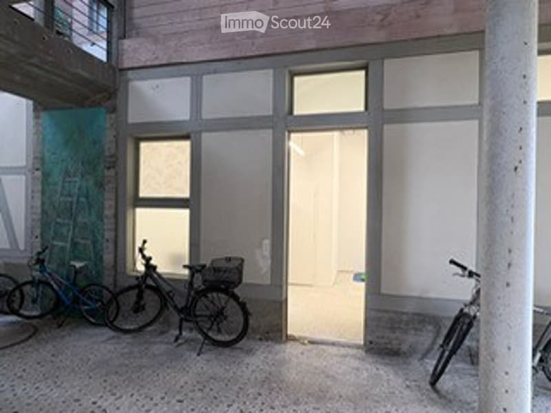 A room with concrete floor, three bicycles parked, open door, windows, and a pillar