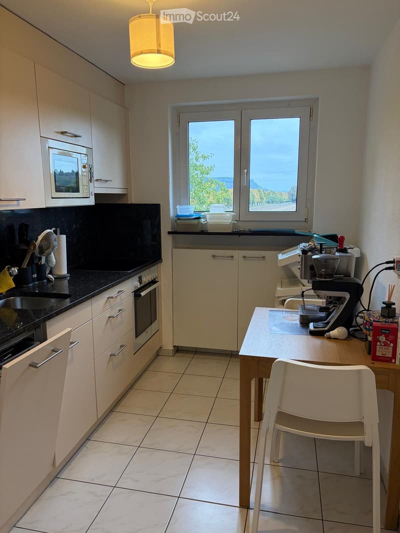 Modern kitchen with white cabinets, black countertops, a microwave, coffee machine, and a small dining area with a table and chair.