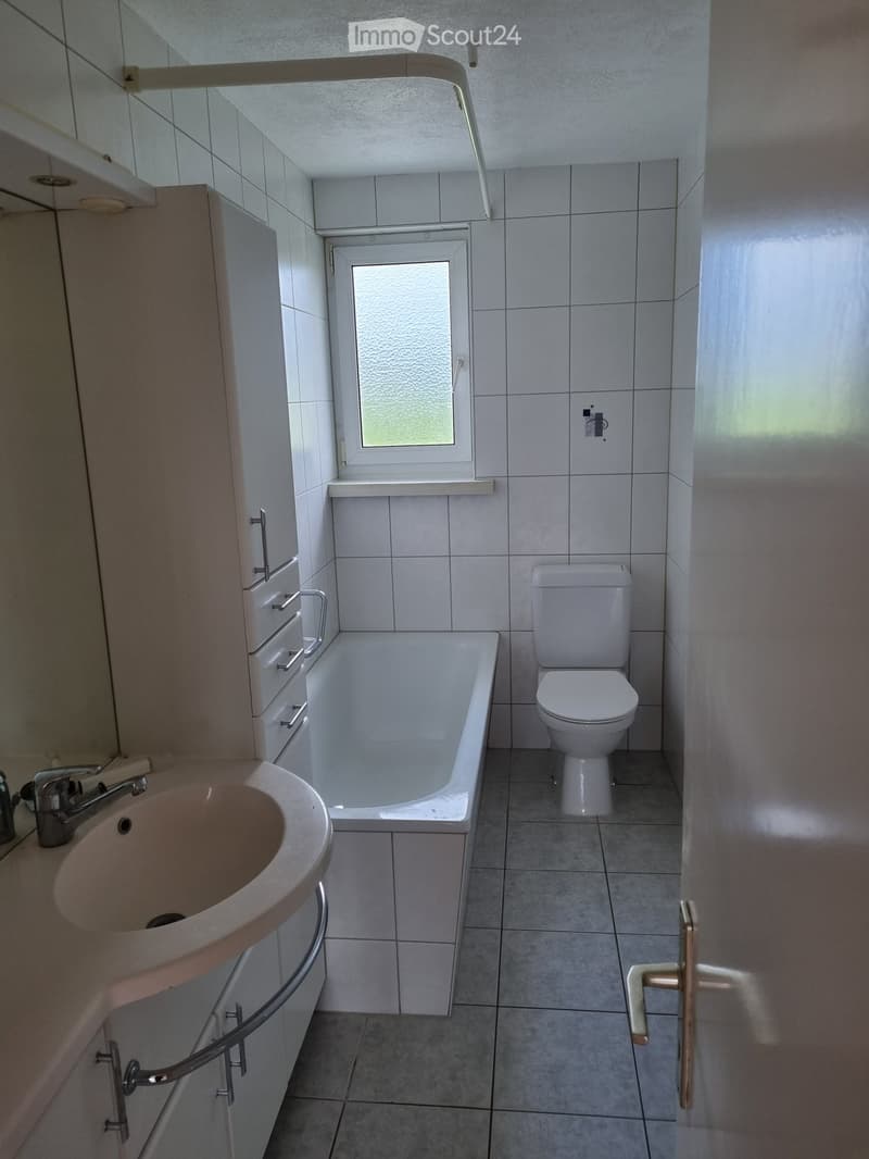 Bathroom with a sink, bathtub, toilet, and cabinet. The room has tiled walls and floor, a window, and a door.