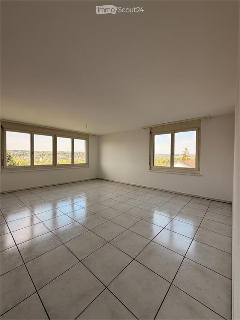 Empty room with tiled floor and large windows offering a view of the landscape.