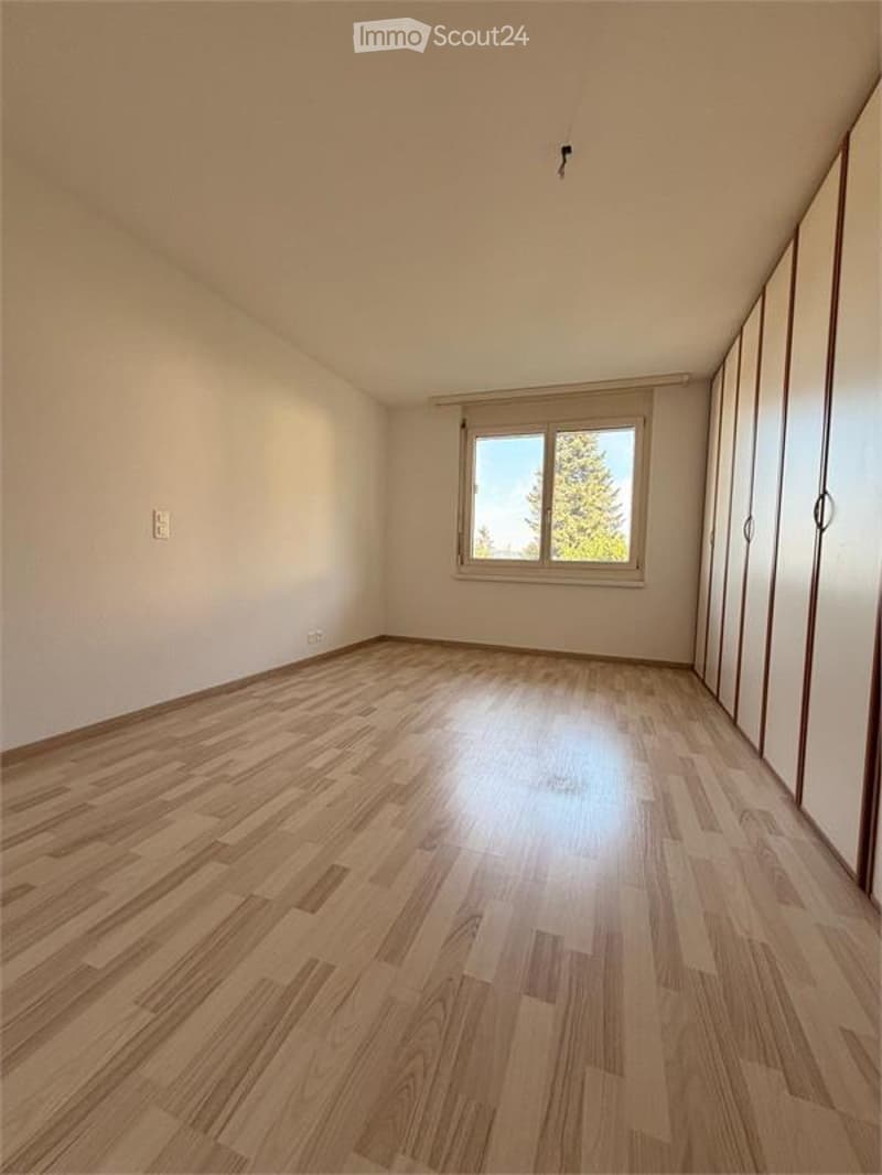 Empty room with wooden flooring, white walls, and a window with a view of trees. No furniture or equipment present.