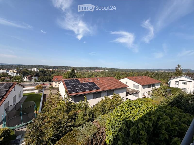 A view from a balcony or terrace overlooking a residential neighborhood with houses, solar panels on roofs, and greenery.