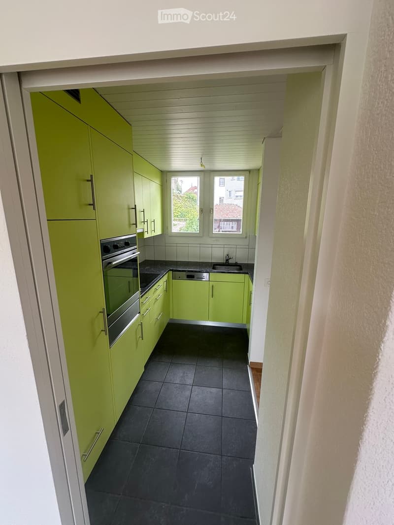 Modern kitchen with green cabinets, stainless steel oven, black countertop, and dark tiled floor.