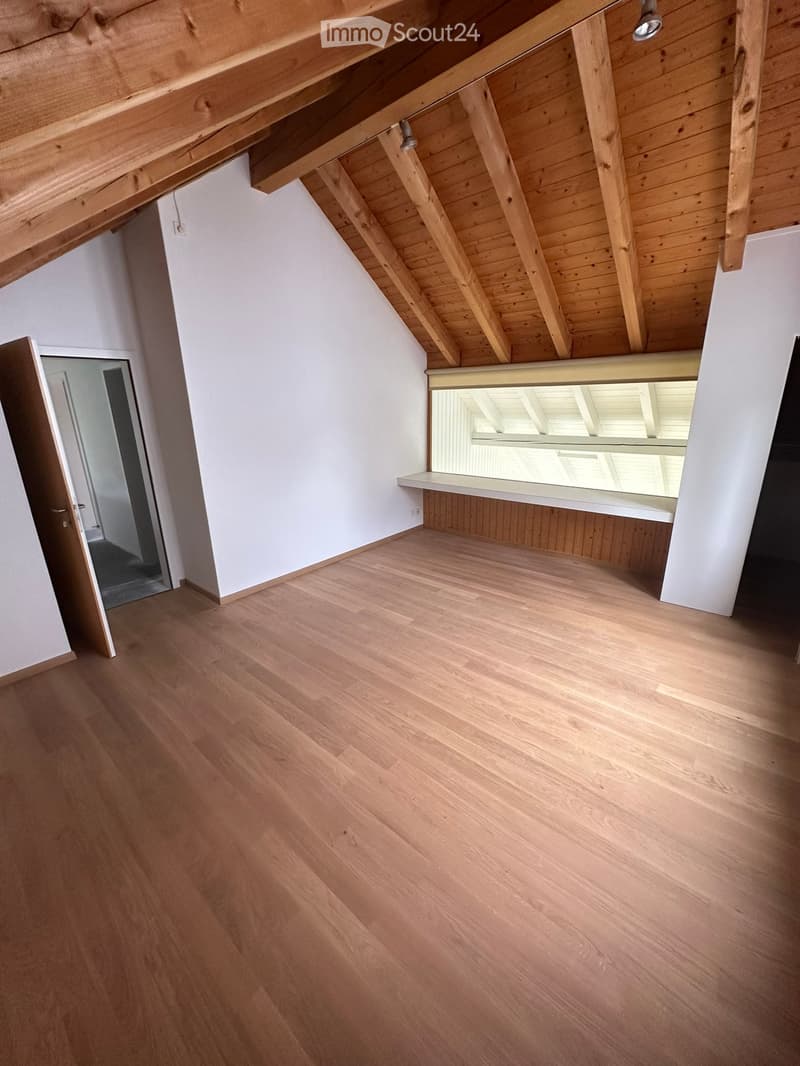 Empty attic room with wooden flooring, white walls, exposed wooden beams, and a skylight window providing natural light.