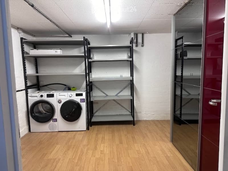 Laundry room with wooden flooring, white walls, two washing machines, metal shelving units, and a mirrored door.