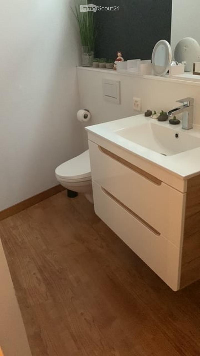 Modern bathroom with a white sink, chrome faucet, mirror, and a toilet. Wooden flooring and white cabinetry.