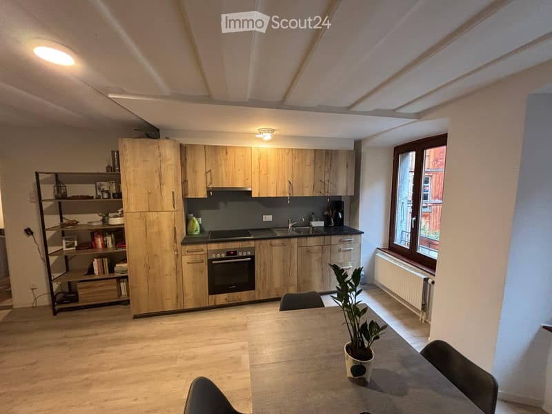 Modern kitchen with light wooden cabinets, stainless steel appliances, a central island, and a dining area with a table and chairs.