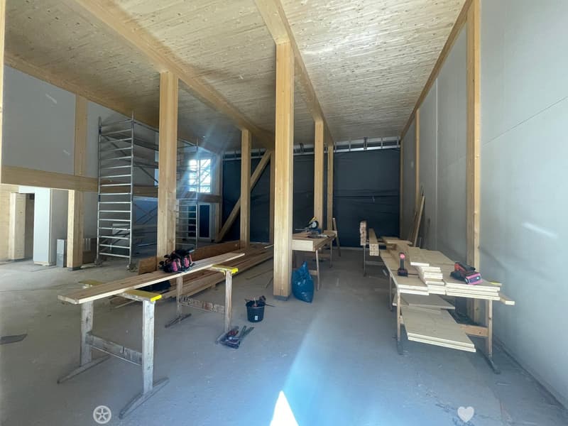 Empty room with exposed wooden beams and construction materials, including workbenches, tools, and lumber.