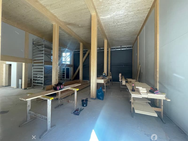 Empty room with exposed wooden beams and construction materials, including workbenches, tools, and lumber.