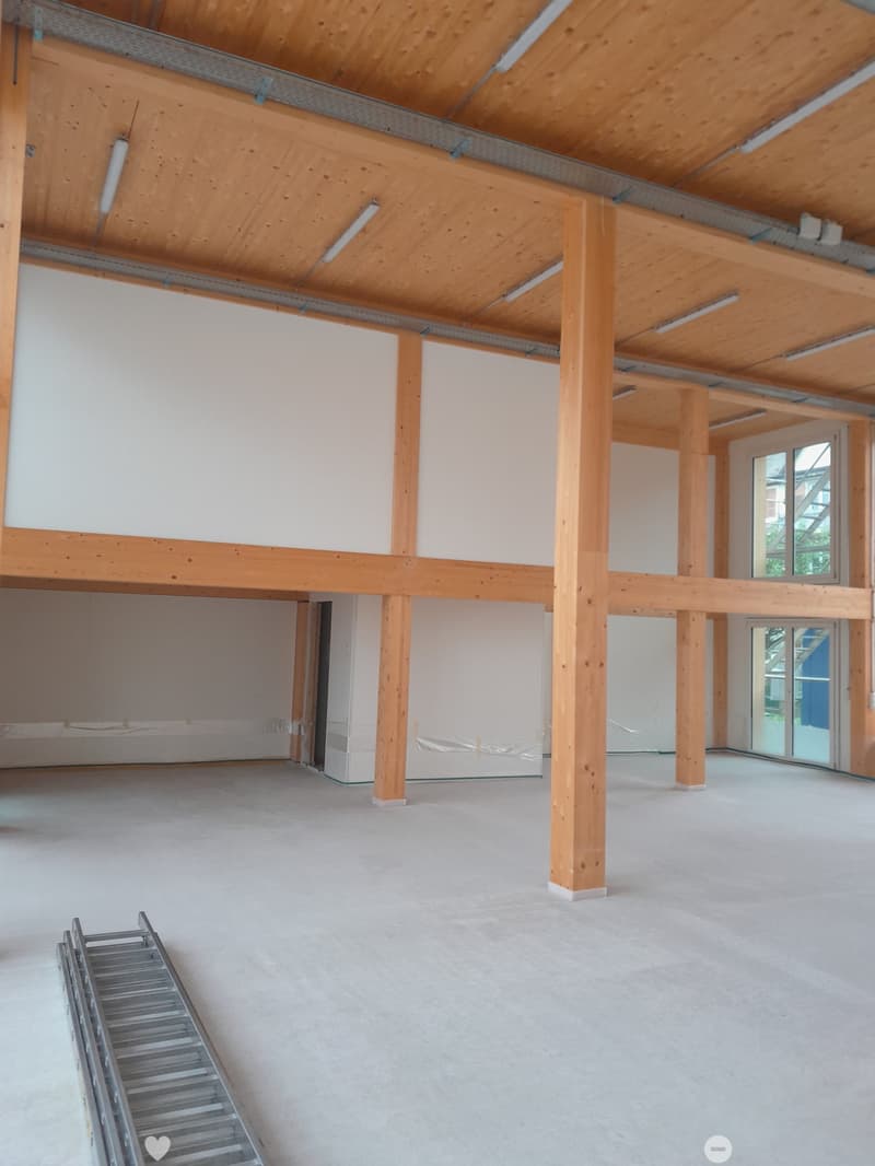 Empty room with exposed wooden beams and pillars, concrete floor, and large windows, showing a raised ground floor structure.