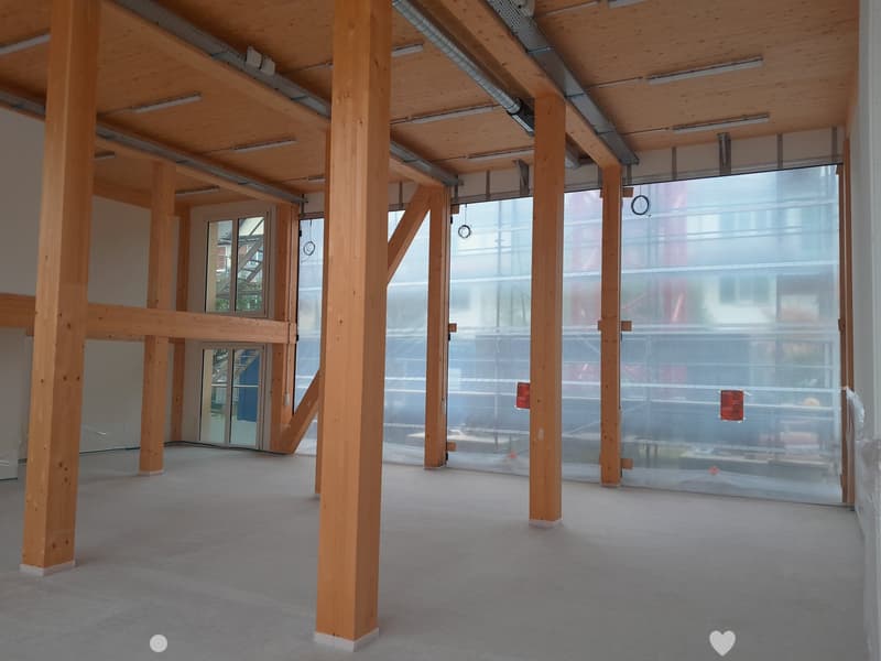 Empty room with wooden beams and pillars, large glass windows, and a carpeted floor.