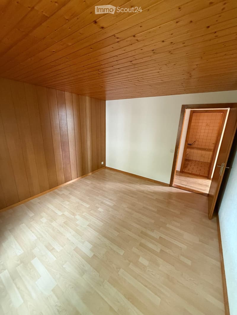 Empty hallway with wooden flooring and paneled wooden walls, leading to a tiled bathroom.