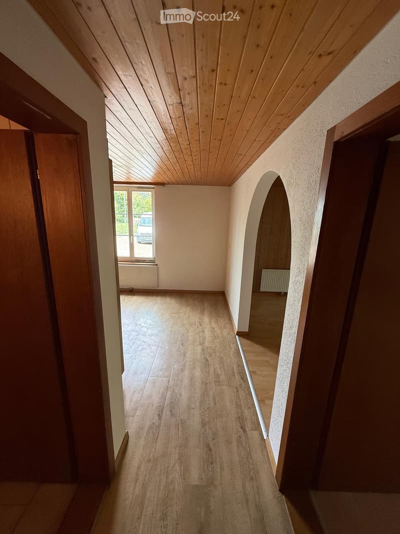 Empty hallway with wooden flooring, arched ceiling, and natural light from a window at the end.