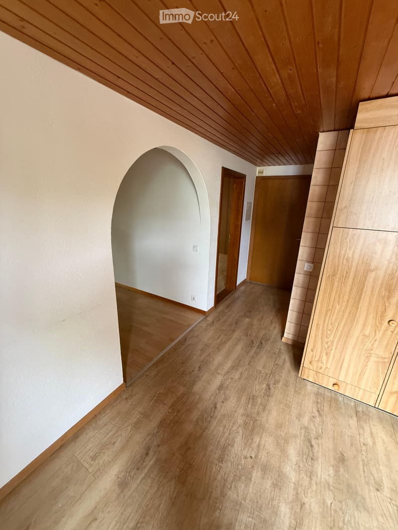 Empty hallway with wooden flooring, white walls, and wooden doors at the end.