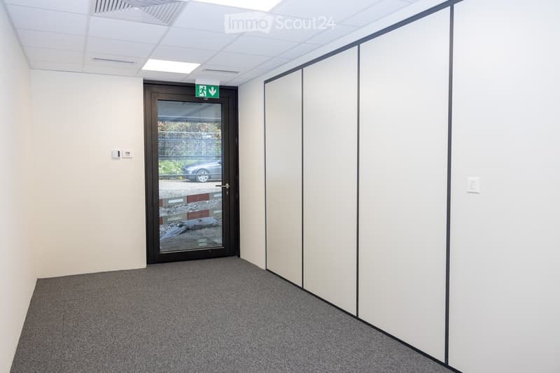 Empty hallway with grey carpet, white walls, a glass door leading outside, and a white partition wall on the right side.