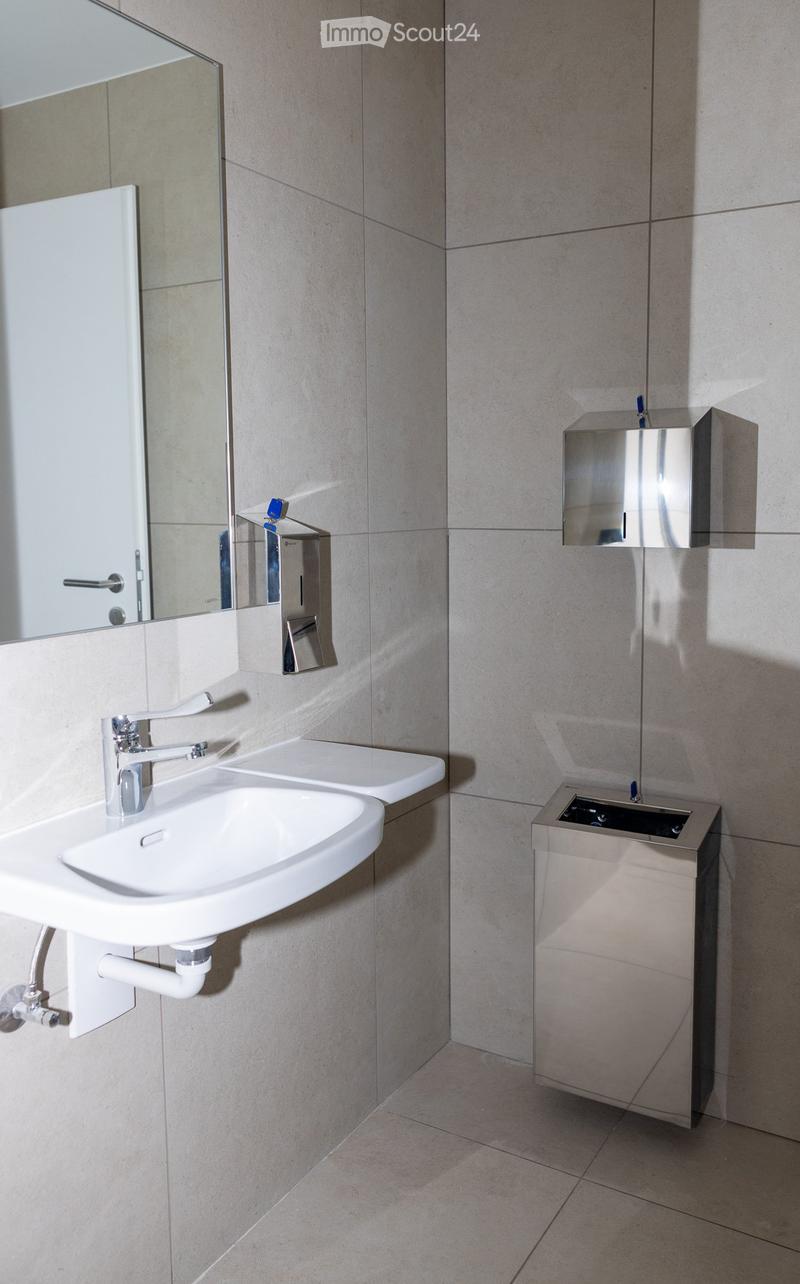 Modern bathroom with a white sink, chrome faucet, mirror, and soap dispensers mounted on beige tiled walls.
