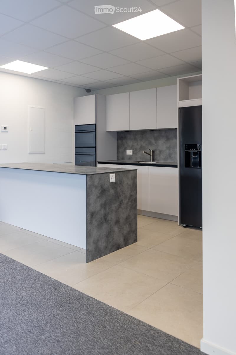 Modern kitchen with white cabinets, a central island, and built-in appliances including an oven and refrigerator. The space features a sleek, contemporary design with a mix of light and dark surfaces.