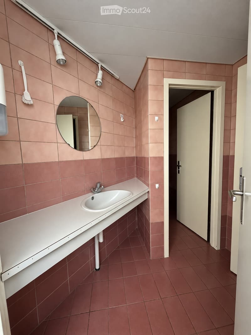 Bathroom with red tiled walls and floor, white countertop sink, round mirror, and mounted light fixtures.