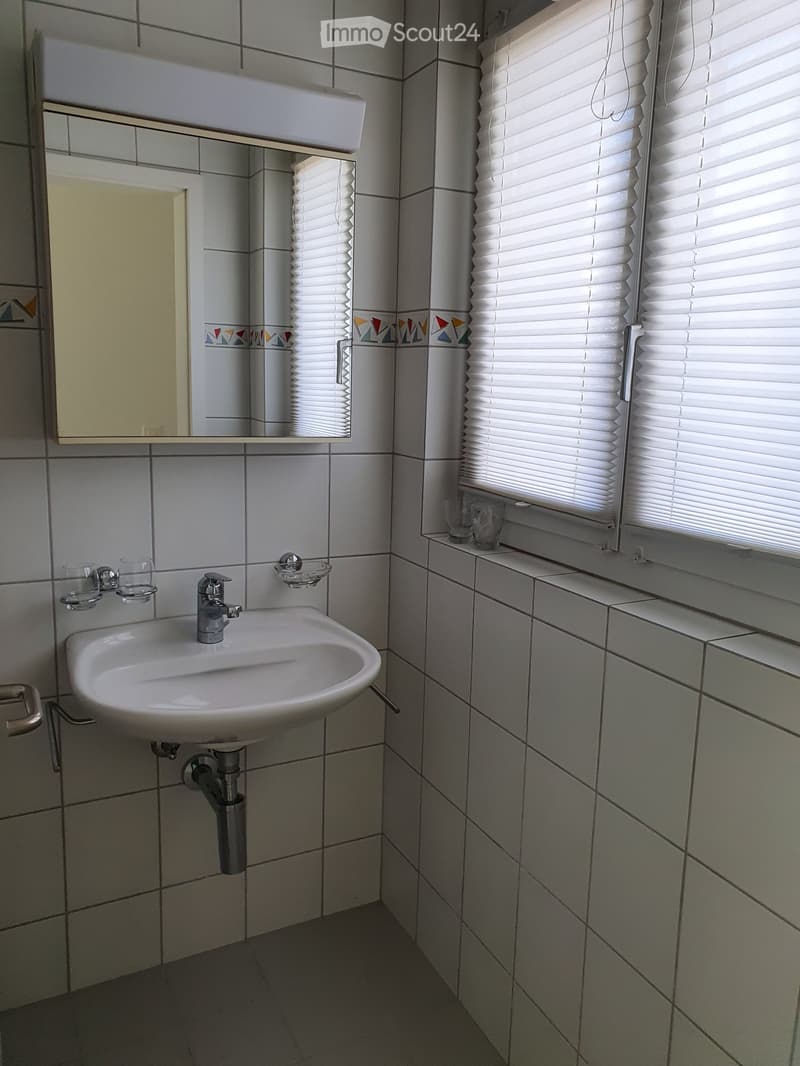 A small bathroom with a white sink, faucet, mirror, and two cups on the counter. The walls are tiled with a decorative border near the top.