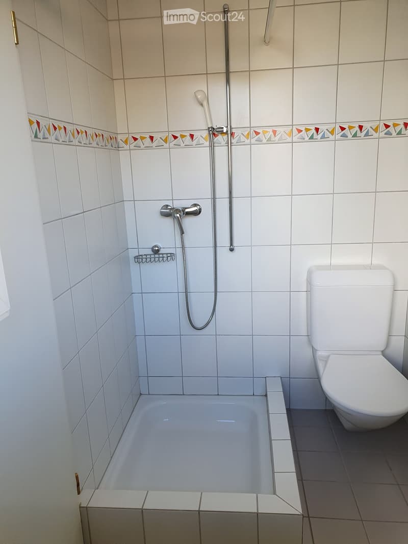 Modern bathroom with white tiles, a bathtub, a toilet, a showerhead, and a small shower rack.