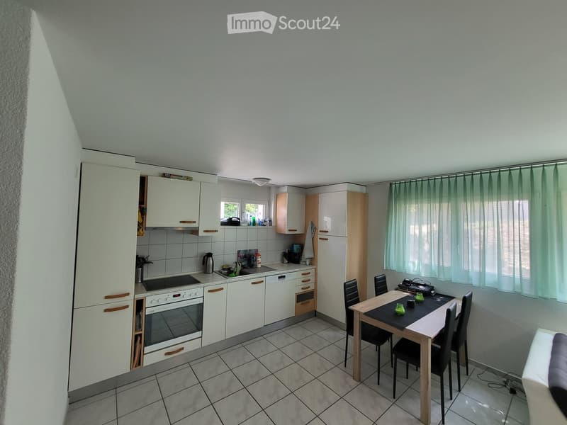 A modern kitchen with white cabinets, a built-in oven, a sink, and a dining area with a table and chairs.