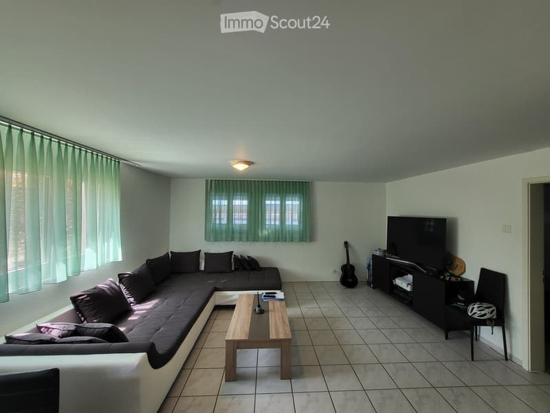 Modern living room with a large sectional sofa, coffee table, TV stand, guitar, and a helmet on a chair.