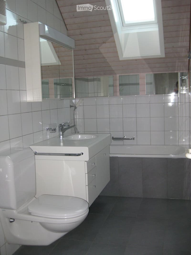 Modern bathroom with white tiles, a toilet, a sink with a faucet, a bathtub, and a large mirror above the sink.
