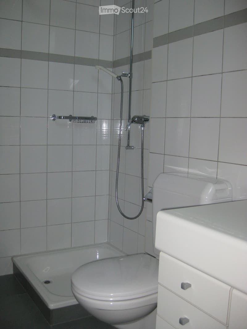 Modern bathroom with a bathtub, toilet, sink, and showerhead. The walls are tiled with light gray tiles and dark gray horizontal stripes.