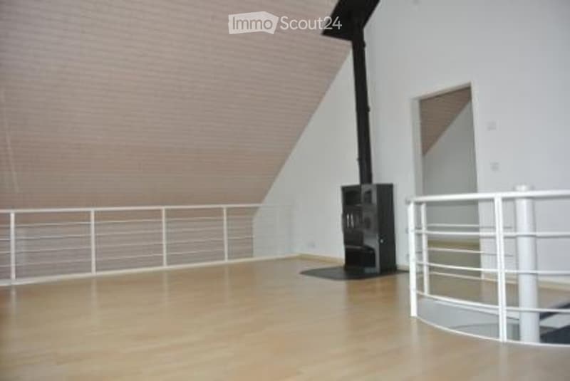 Completely empty room with wooden floor, white walls, and a black fireplace. The room has a white metal railing along the edge of the raised floor.