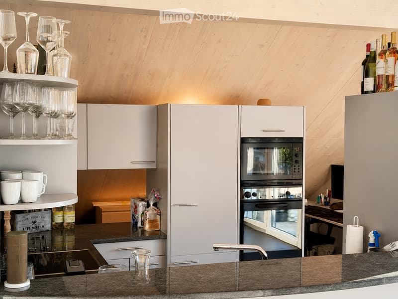 Modern kitchen with white cabinets, stainless steel appliances, and wooden accents. Features include a built-in oven, a sink with a modern faucet, and open shelving displaying wine glasses and cups.