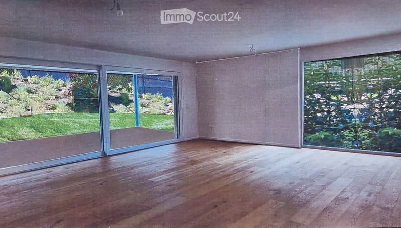 Empty room with wooden flooring, large sliding glass doors, and natural light from the garden view.
