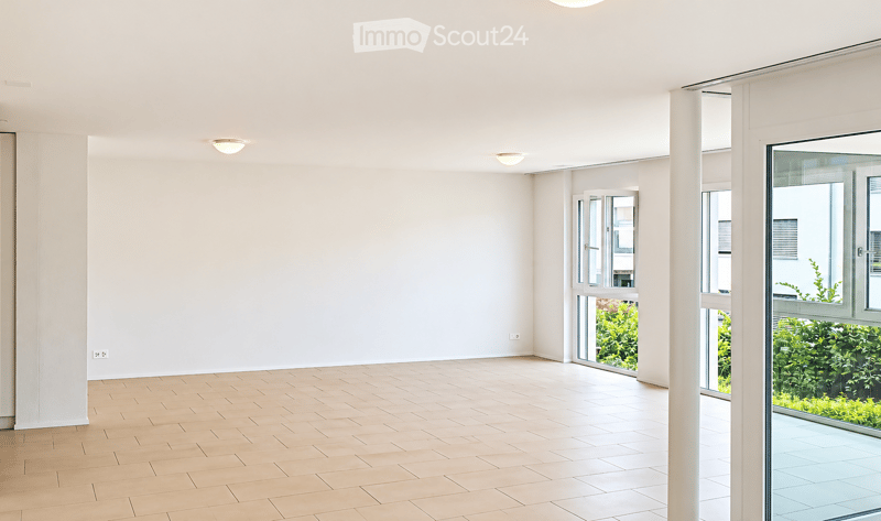 Empty room with light wooden flooring, white walls, and large windows with sliding glass doors leading to a balcony area.