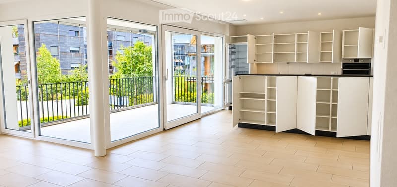 Bright, unfurnished room with large sliding glass doors leading to a balcony, white tiled floor, and white kitchen cabinets.
