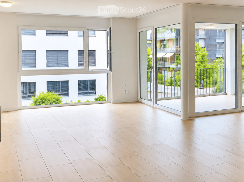 Empty room with light wooden flooring, large windows, and sliding glass doors leading to a balcony.