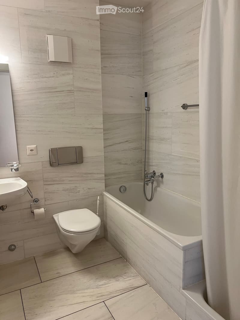 Modern bathroom with marble walls and floor, featuring a toilet, bathtub, sink, and showerhead.