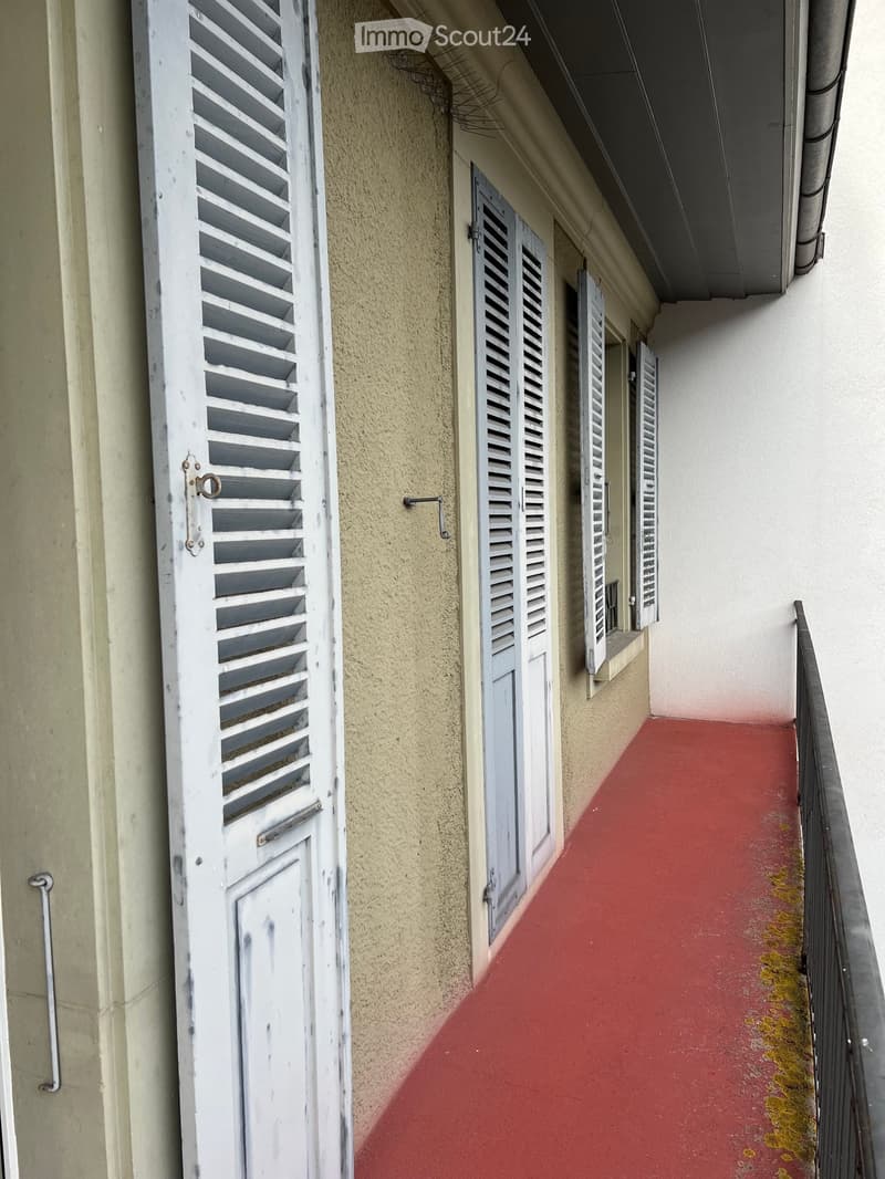 Balcony with red flooring, white shutters, and a small ledge with a window.