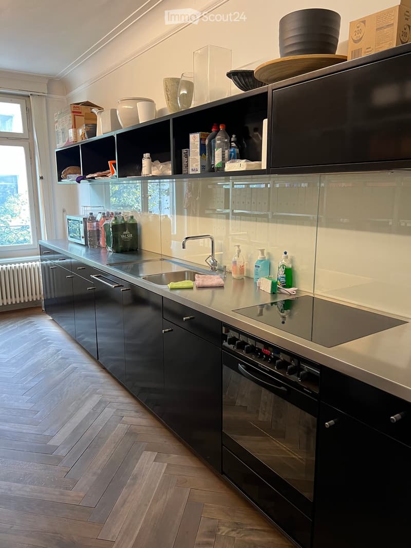 Modern kitchen with dark cabinets, stainless steel appliances, and a central island with a sink and faucet. The countertop features various items including bottles, a bowl, and cleaning supplies.