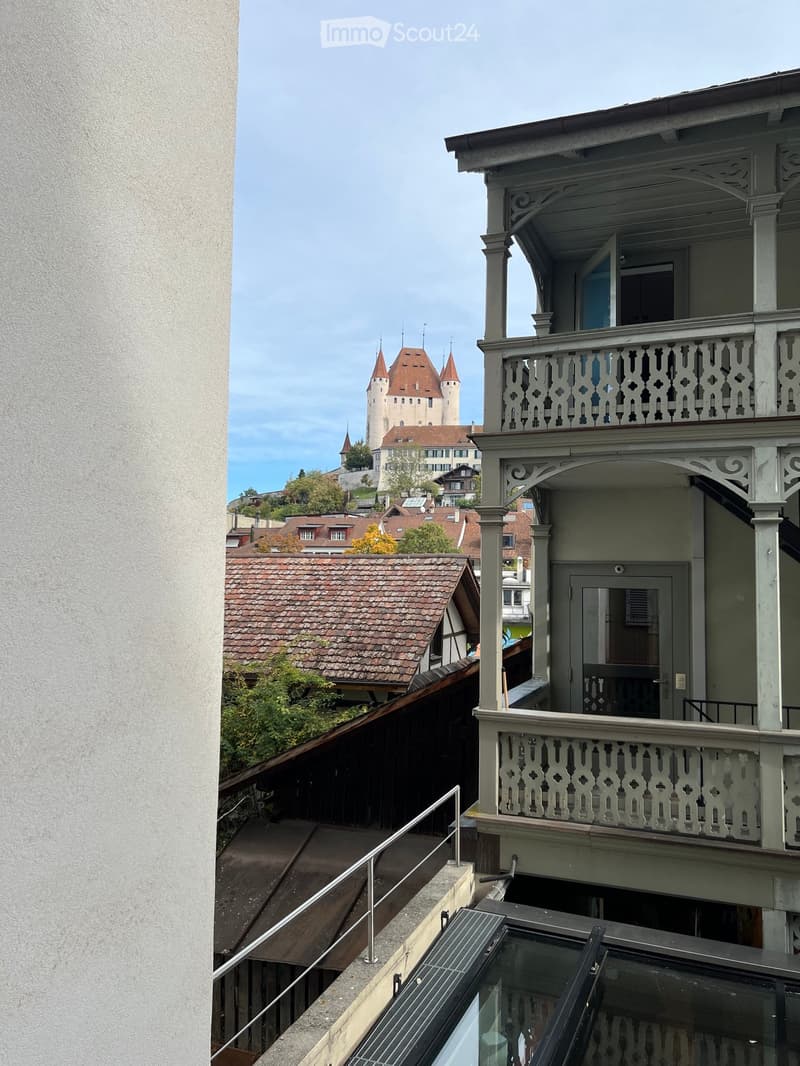 Balcony with ornate white railing, overlooking a historic town with a castle and traditional houses.