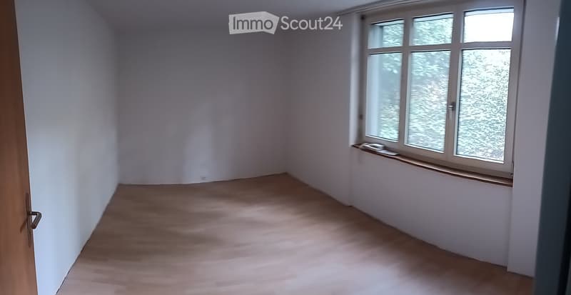 Empty room with light wooden flooring and white walls, featuring a large window with frosted glass panes and a small wooden sill.