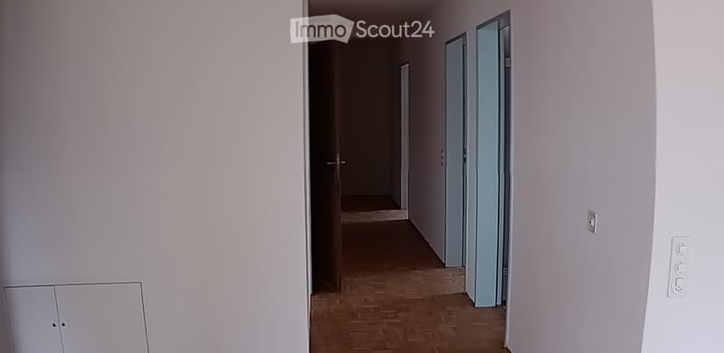 Empty hallway with light-colored walls, wooden flooring, and two doors leading to other rooms.