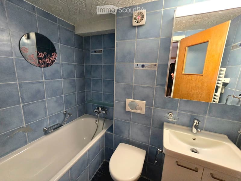 Bathroom with blue tiled walls, a bathtub, toilet, sink, and a wooden cabinet with a mirror.