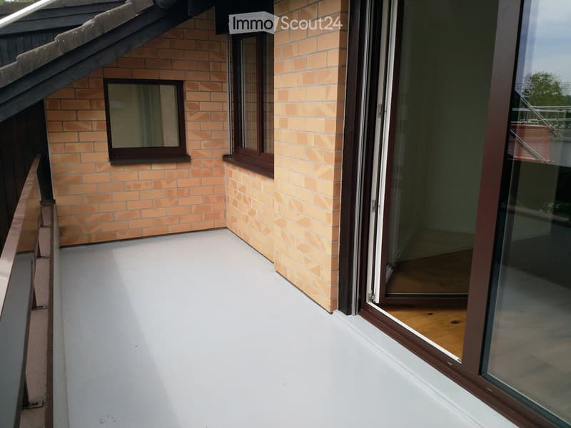 Balcony with light-colored flooring, brick walls, and large glass doors leading inside.