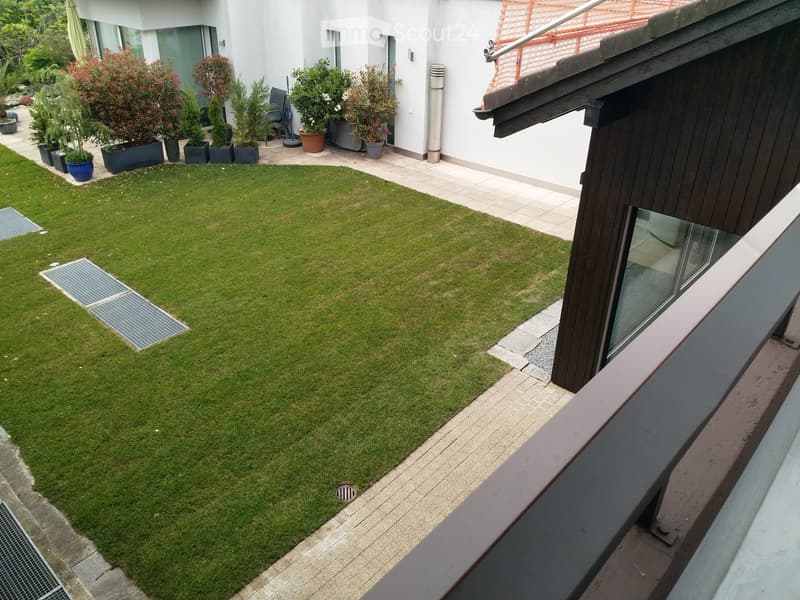 Well-maintained garden with a neatly trimmed lawn, surrounded by a paved pathway and potted plants near the building entrance.