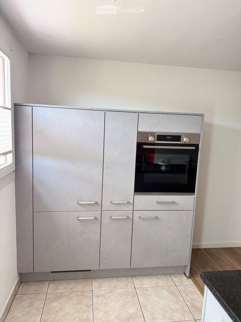 Modern kitchen with grey cabinets, an integrated oven, and tiled flooring.